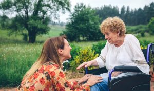 A young woman talks with a woman in a wheelchair in an outdoor setting